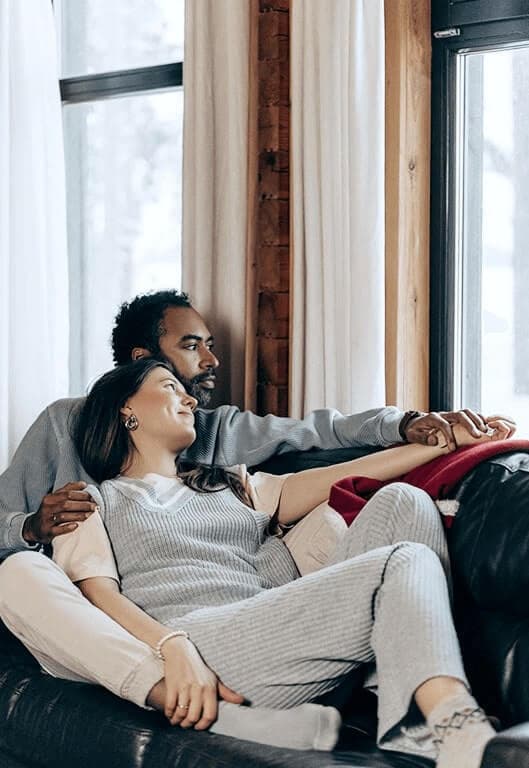 Mann und Frau liegen Arm in Arm auf dem Sofa und schauen aus dem Fenster