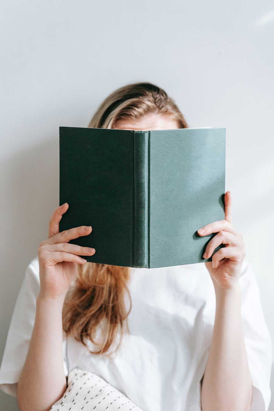 Frau liest ein Buch und dabei wird ihr Gesicht verdeckt.