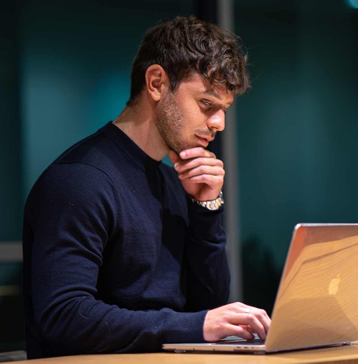 Junger Mann der nachdenkend vor einem Laptop steht