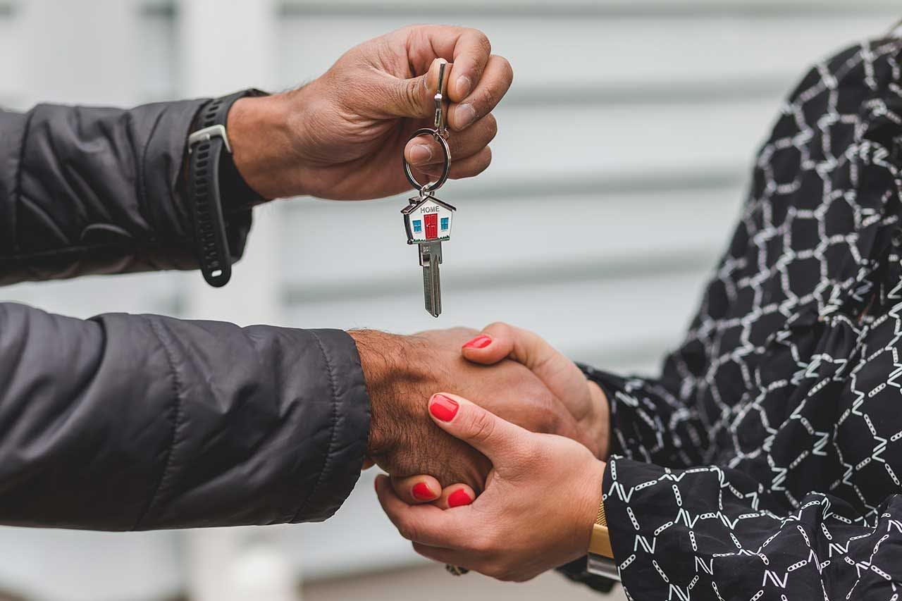 Eine Person überreicht der anderen Person einen Hausschlüssels des neu gekauften Hauses, welches mit einer Baufinanzierung finanziert worden ist.